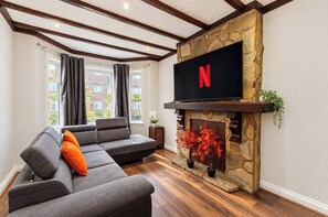 A living room with a stone fireplace, a flat-screen TV, and a grey sectional sofa. - 4BR Wembley Stay w/ Pool Table & Free Parking (Greater London)