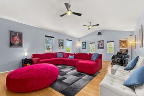 A spacious living room with a red sectional sofa, a grey and black rug, and a white armchair. - Private Pool & Loungers | Theater, Dry Sauna & Games (San Antonio)