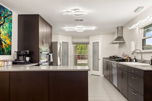 A modern kitchen with dark cabinetry, a large island, and a view to the outside. - Private Pool & Loungers | Theater, Dry Sauna & Games (San Antonio)