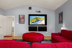 A living room with a flat-screen TV mounted on the wall, red sofas, and a red bean bag chair. - Private Pool & Loungers | Theater, Dry Sauna & Games (San Antonio)