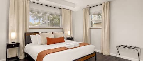 Quarto com cama, mesas de cabeceira, ventoinha no teto e janela com cortinas.