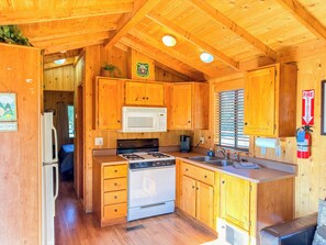 Cocina compacta con armarios de madera, microondas, estufa y pileta.