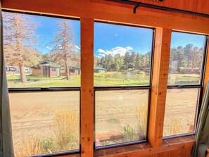 Una habitación con ventanas amplias que ofrecen vistas a un área verde, árboles y un edificio distante.