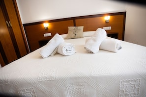 A neatly made bed with rolled white towels, a wooden headboard, and a wall-mounted light fixture. - LLANOS 8 APARTMENT (Cuevas del Almanzora)