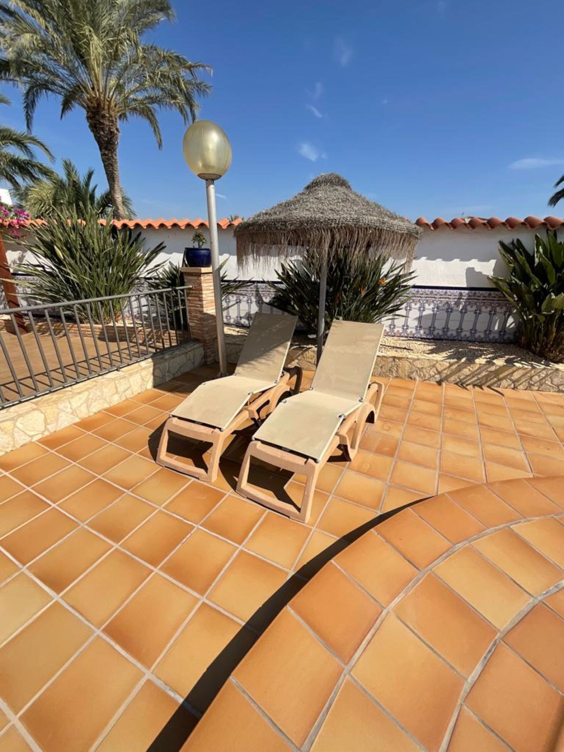 A patio with lounge chairs, a thatched-roof structure, and a tiled floor.