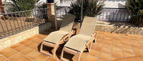 Une terrasse avec des chaises longues, une structure à toit de chaume et un sol carrelé.