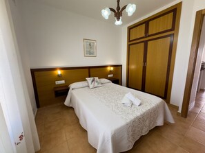Quarto de hotel com uma cama de casal, cabeceira de madeira, mesa de cabeceira, guarda-roupa e luminária no teto.