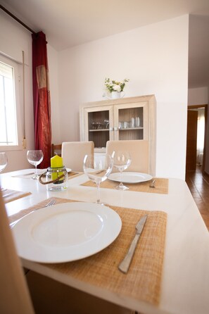 A dining table set with white plates, wine glasses, and cutlery, with a wooden cabinet in the background. - LLANOS 5 APARTMENT (Cuevas del Almanzora)