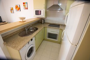 A compact kitchen with a washing machine, microwave, and stove. - LLANOS 4 APARTMENT (Cuevas del Almanzora)