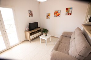 A living room with a beige sofa, a white coffee table, a TV on a wooden stand, and three wall-mounted paintings. - LLANOS 4 APARTMENT (Cuevas del Almanzora)