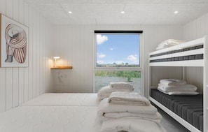A bedroom with a bunk bed, a bedside table with a lamp, a window with a view of the outdoors, and a painting on the wall. - Beautiful home in Idestrup with sauna (Idestrup)
