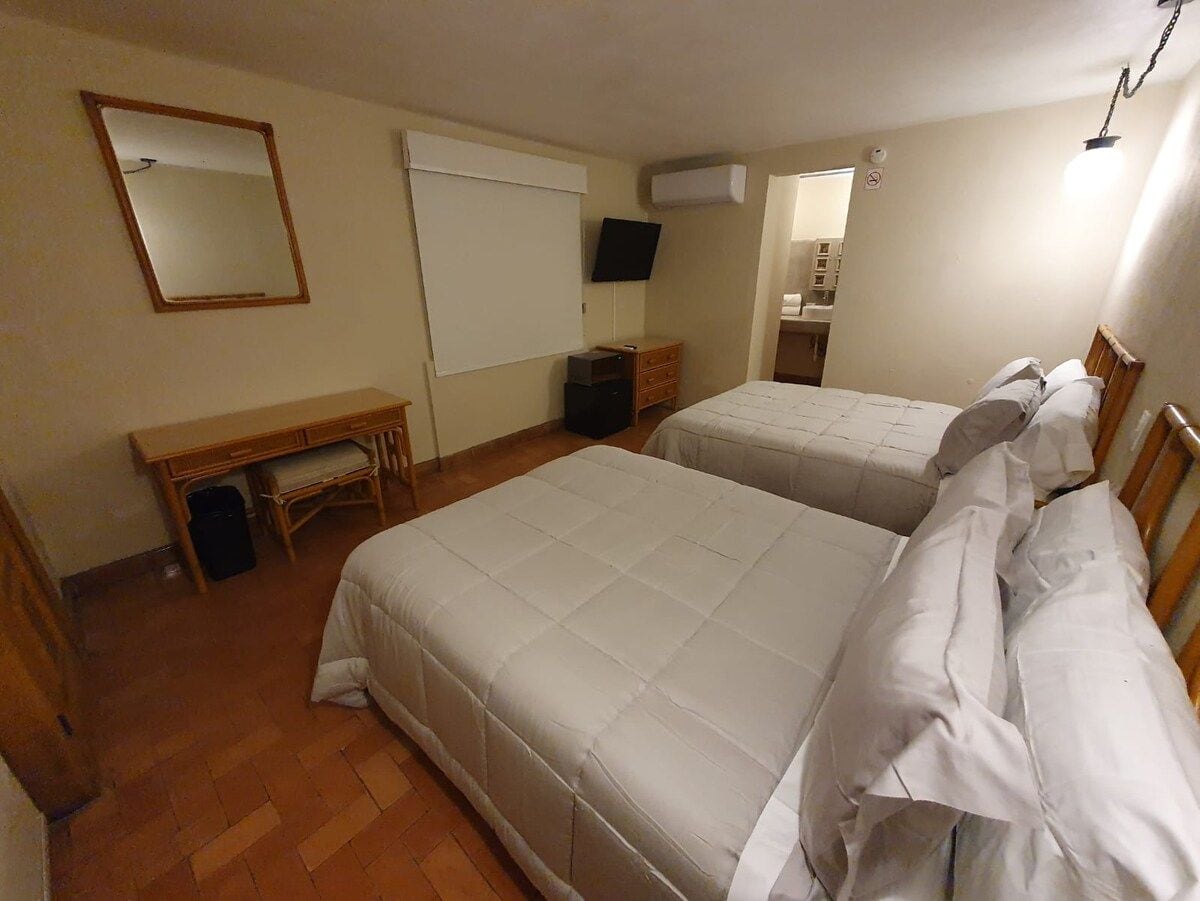 Habitación de hotel con dos camas, un escritorio, una silla, un espejo, un televisor y una ventana.