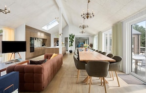 Eine moderne Küche mit einer großen Kochinsel, einem Essbereich mit langem Tisch und Stühlen und einer gemütlichen Sitzecke mit einer Couch und Sesseln.