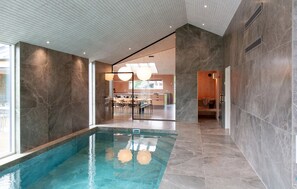 An indoor swimming pool with a modern design, a kitchen area visible through a glass partition, and a sauna area. - Gorgeous home in Højslev with sauna (Højslev)