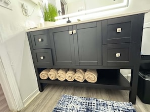 A bathroom with a dark-colored vanity, a mirror, and a shelf with rolled towels. - Waterfront Retreat in Jacksonville (Jacksonville)