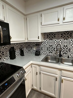 A kitchen with white cabinets, a black and white patterned backsplash, a stainless steel sink, and a black coffee maker. - Waterfront Retreat in Jacksonville (Jacksonville)