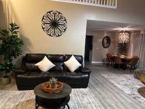 A living room with a black leather sofa, a coffee table, and a dining area with chairs and a chandelier. - Waterfront Retreat in Jacksonville (Jacksonville)