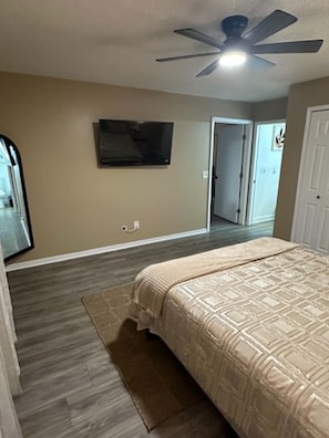 A bedroom with a bed, a ceiling fan, a TV mounted on the wall, and a door leading to another room. - Waterfront Retreat in Jacksonville (Jacksonville)