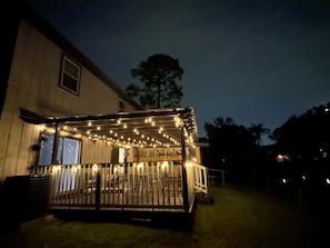 A covered outdoor seating area with string lights, a metal railing, and a house in the background. - Waterfront Retreat in Jacksonville (Jacksonville)
