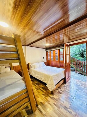 Un interno in legno con un letto, una scala di legno e vista su uno spazio esterno attraverso una porta.