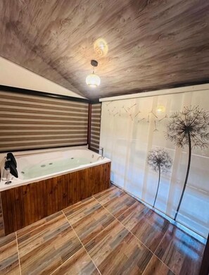 Un bagno moderno con pavimento in legno, una vasca da bagno indipendente e una parete decorativa con arte astratta.