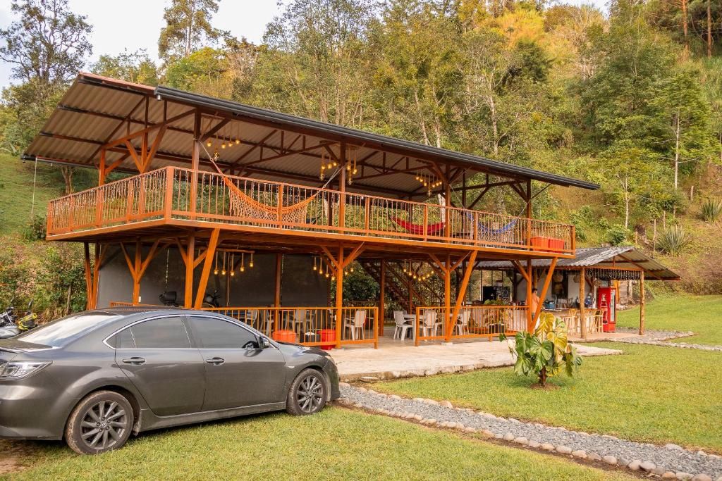 Un edificio de dos pisos con balcón, zona de estar al aire libre y un coche estacionado frente a él.