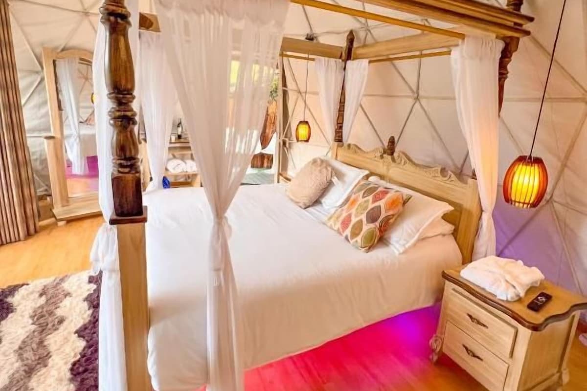 Un letto a baldacchino con tenda, un comodino e un tavolino da notte in una stanza a forma di tenda con pavimento in legno.