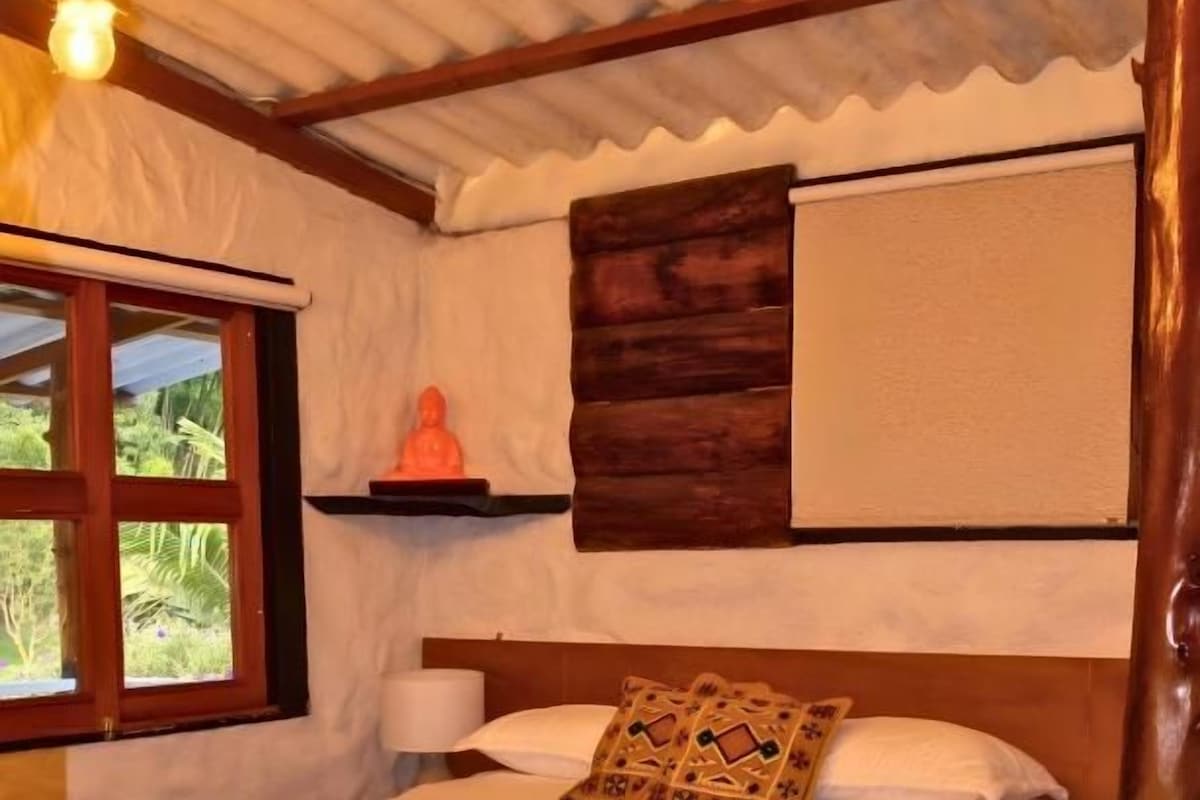 Un letto singolo con testiera in legno, una finestra vista verde e uno scaffale a parete con una statua.
