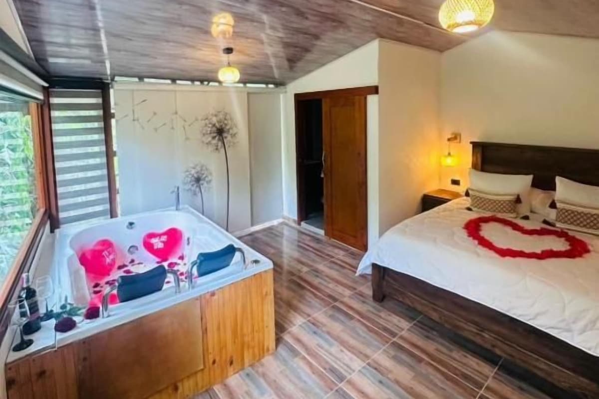 Una stanza con soffitto in legno, un letto grande decorato con un cuore, e una vasca da bagno in legno separata, anch'essa decorata con un cuore.