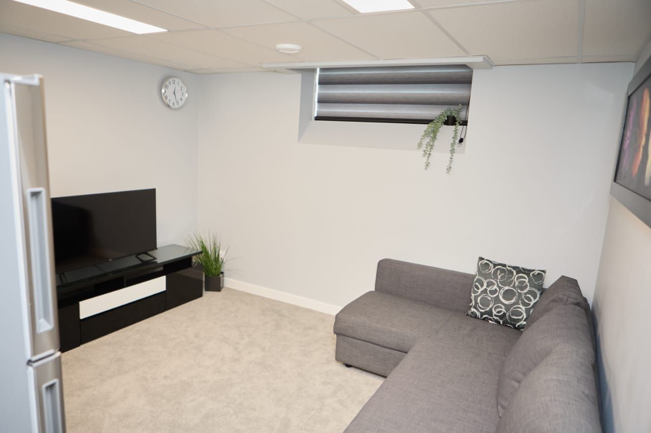 A modern living room with a flat-screen TV, a grey sofa, a small plant, and a clock on the wall.