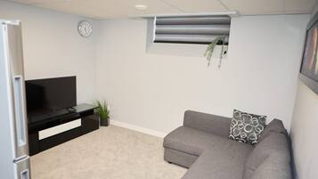 A modern living room with a flat-screen TV, a grey sofa, a small plant, and a clock on the wall.