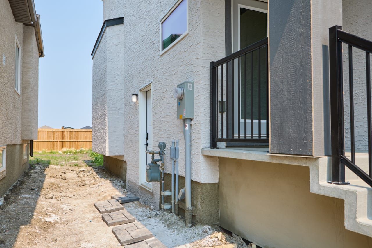 A narrow outdoor pathway leading to a building with a black metal railing and a utility box.