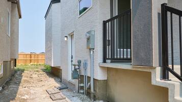 A narrow outdoor pathway leading to a building with a black metal railing and a utility box.