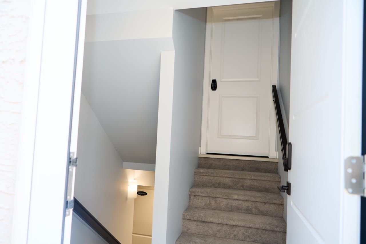 A staircase leading to a white door with a black handle, carpeted steps, and a light fixture on the wall.