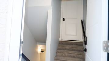 A staircase leading to a white door with a black handle, carpeted steps, and a light fixture on the wall.