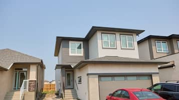 A two-story residential building with a garage, a red car parked in front, and a clear sky.