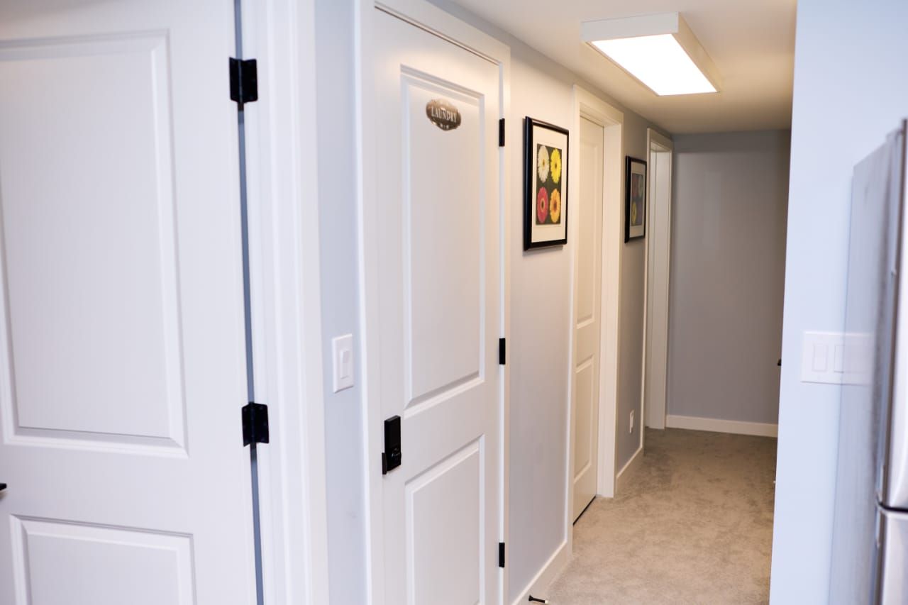 A hallway with white doors, a framed picture on the wall, and a refrigerator on the right.
