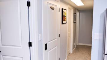 A hallway with white doors, a framed picture on the wall, and a refrigerator on the right.