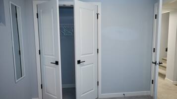 A room with two white doors, one open revealing a closet with hanging clothes, and a carpeted floor.
