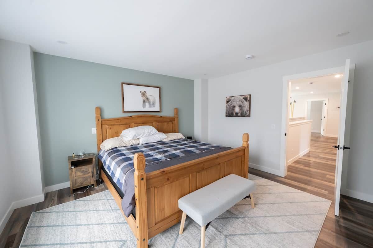 A bedroom with a wooden bed, a bench, a nightstand, and a door leading to another room.