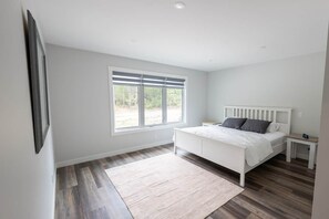 A bedroom with a bed, a nightstand, a window, and a wall-mounted picture.