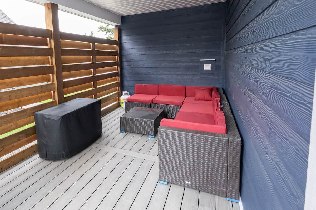 Un patio al aire libre con un sofá rojo, dos mesas pequeñas y un banco cubierto.