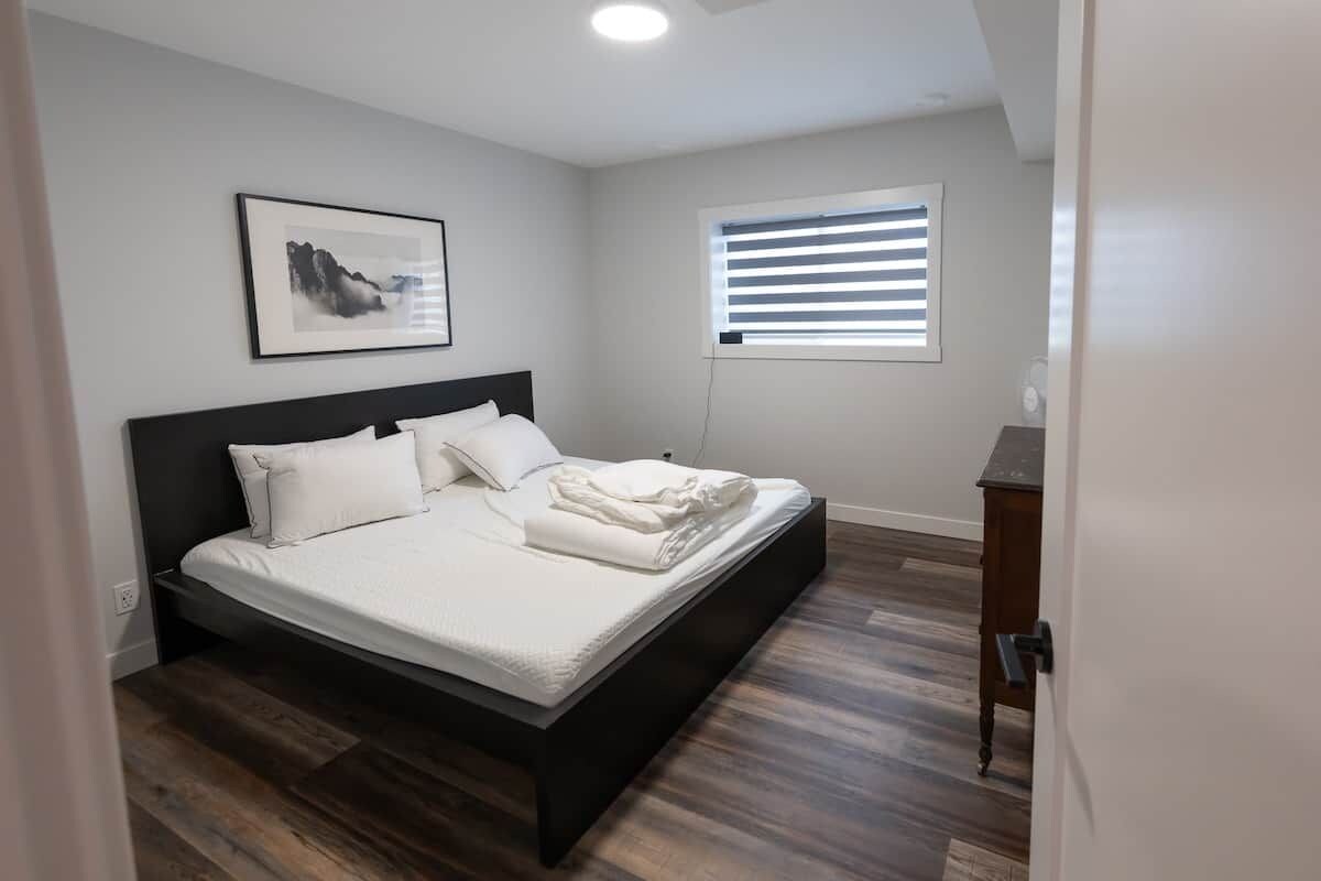 A bedroom with a bed, a window with blinds, a wall-mounted picture, and a wooden floor.