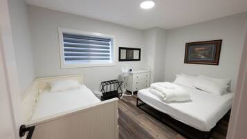Un dormitorio con dos camas, una ventana con persianas, una mesita de noche con lámpara y un cuadro en la pared.