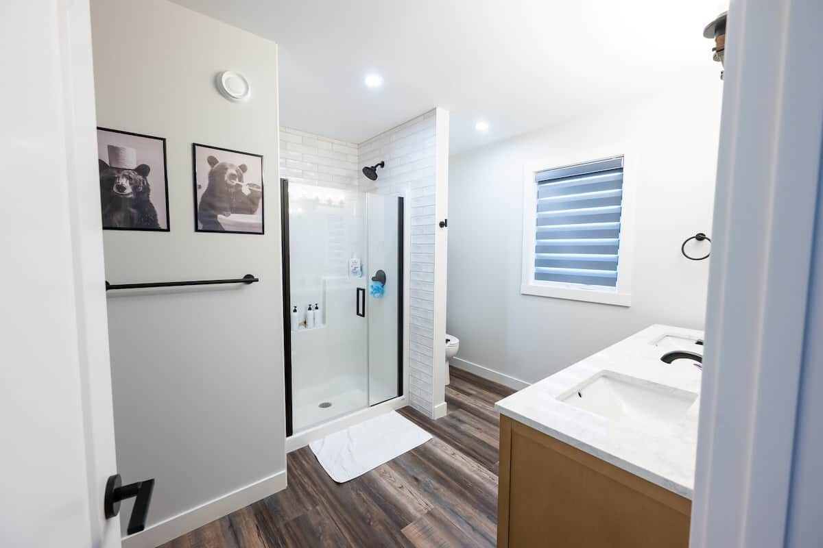 Un baño moderno con cabina de ducha de vidrio, lavamanos blanco y ventana con persianas.