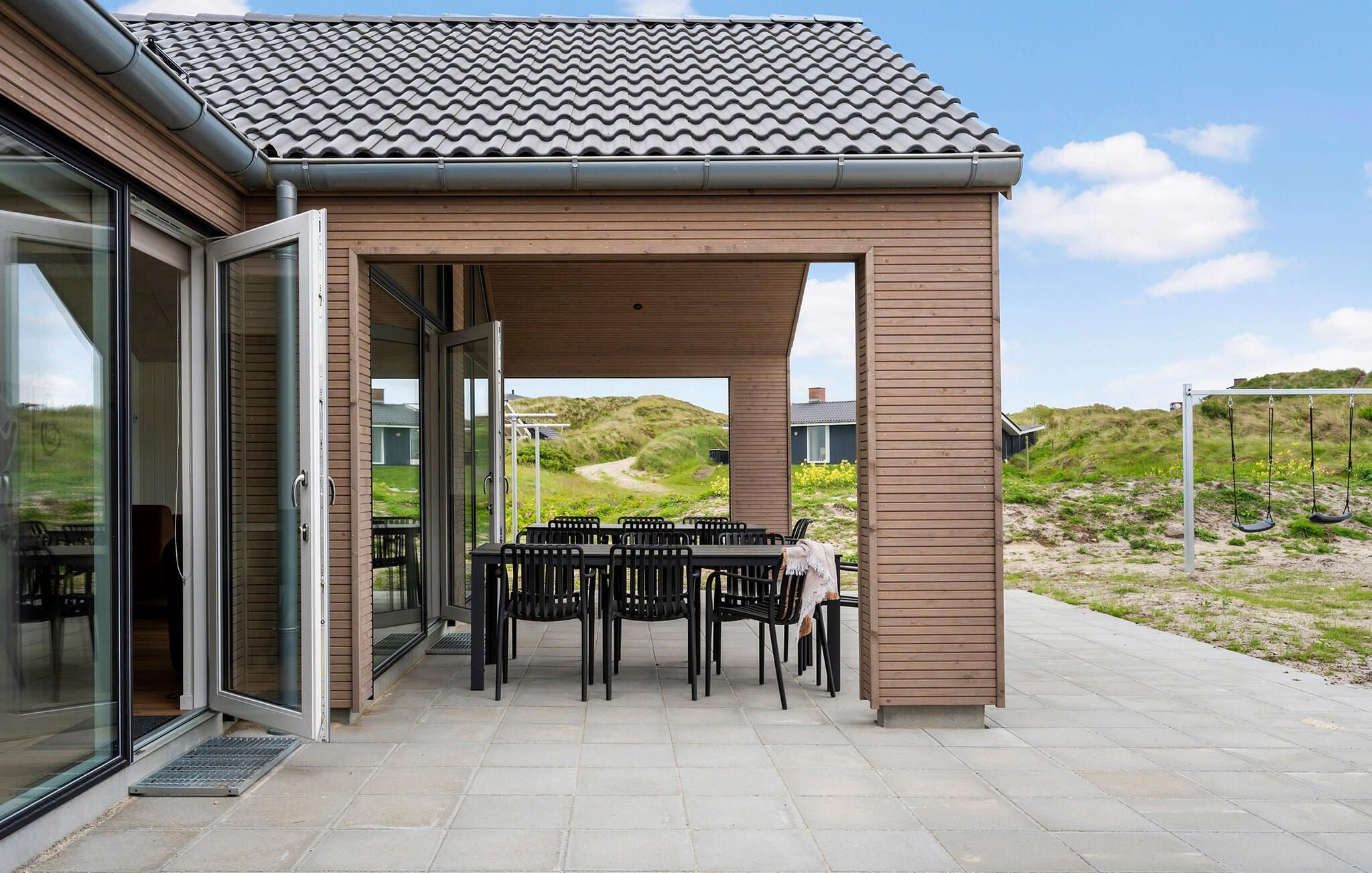 Een overdekt terras met een tafel, stoelen, een houten pergola en uitzicht op het landschap.