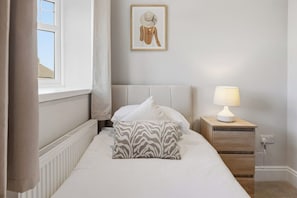 A bedroom with a bed, a nightstand with a lamp, a radiator, a window with curtains, and a framed picture on the wall. - Luxury 4-Bed Contractor/Family House Sleeps 7 (Cheshire West and Chester)
