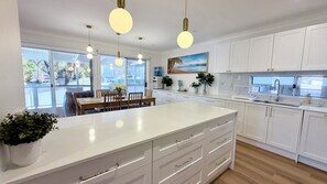 A modern kitchen with white cabinetry, a large island, and pendant lighting. - Holiday House Southport near Surfers Paradise. (Southport)
