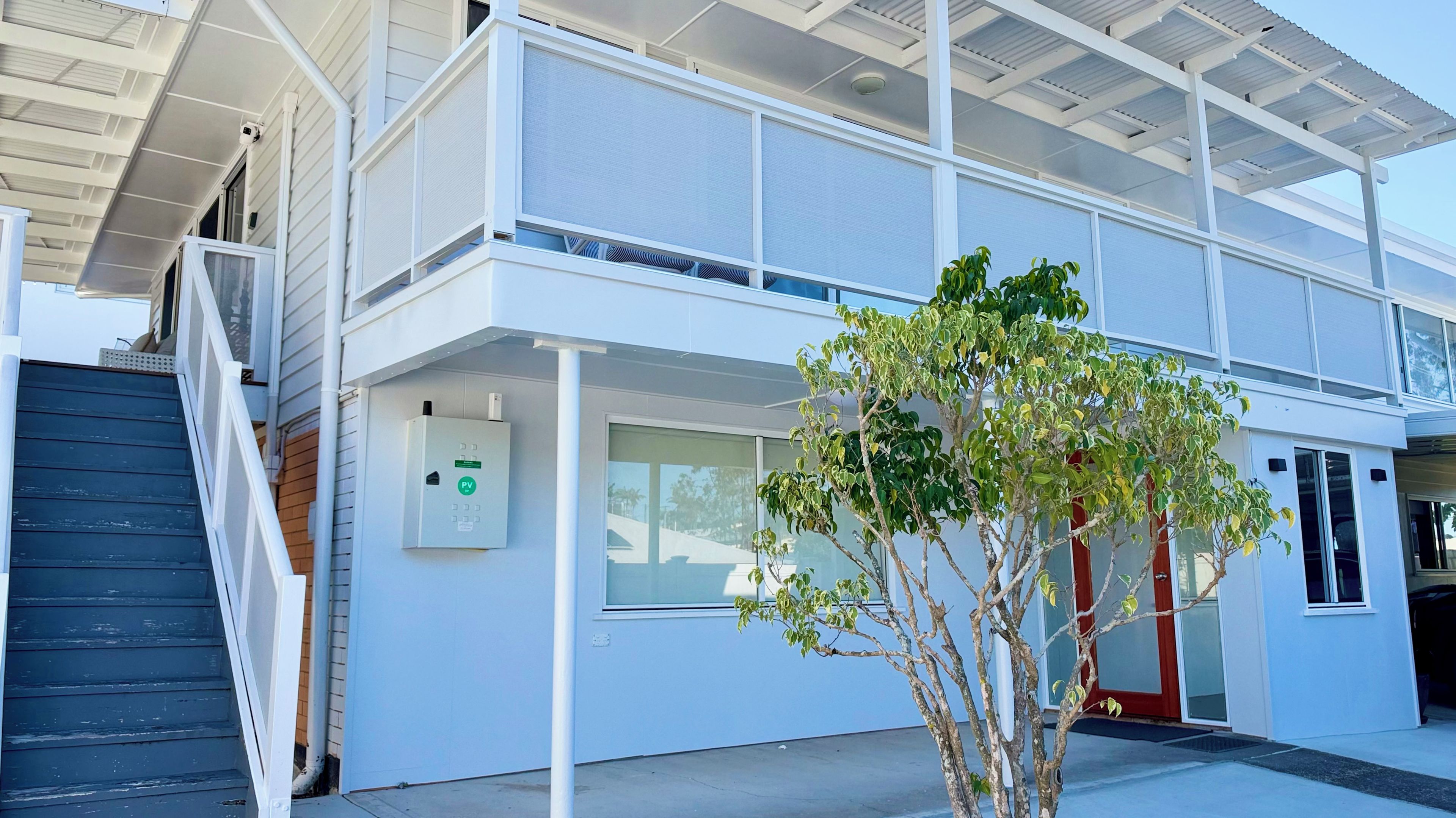 A modern two-story building with a covered outdoor area, a staircase, and a small tree.