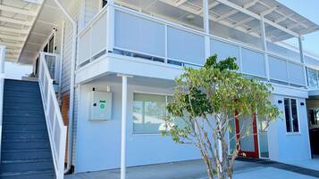 A modern two-story building with a covered outdoor area, a staircase, and a small tree.